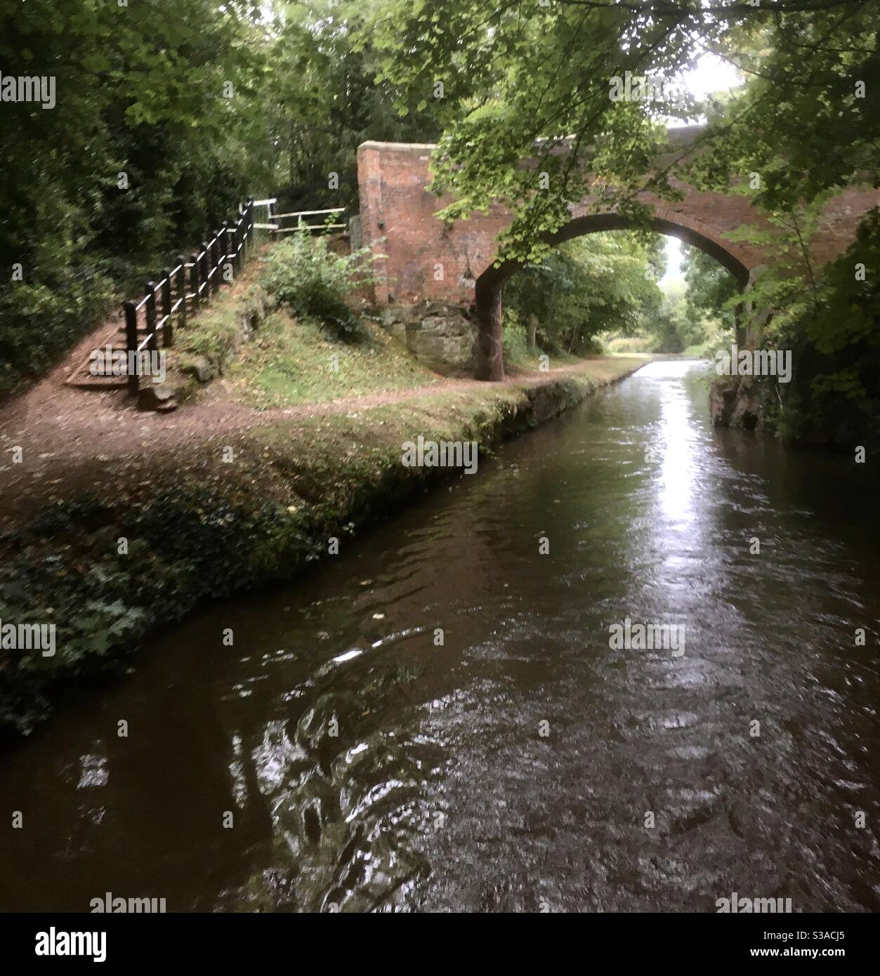 Vista sul canale che mostra un ponte ad arco in mattoni che attraversa il canale l'alzaia e un sentiero in periplo per attraversare il ponte. Foto scattata dalla parte posteriore di una barca a mezzaluna. - Immagine stock catturata con smartphone