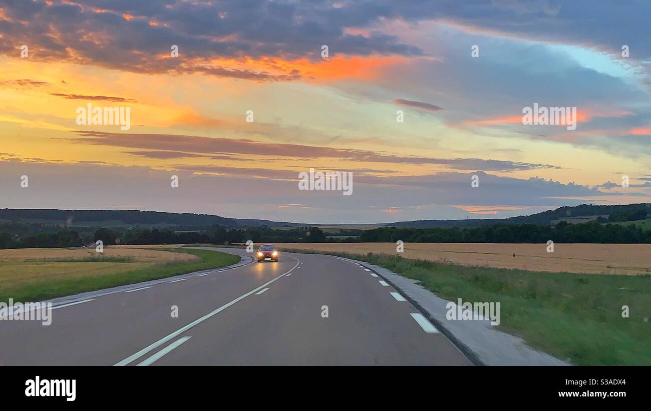 Auto su una strada al tramonto Foto Stock