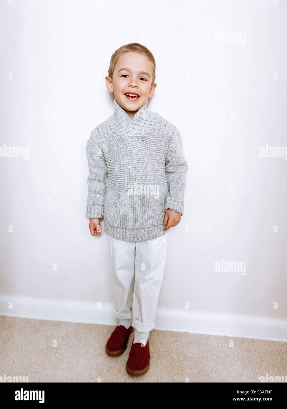 Piccolo biondo che pose per una foto il giorno di Pasqua nel 2020 in un maglione grigio in maglia, pantaloni bianchi e mocassini marroni. Foto Stock