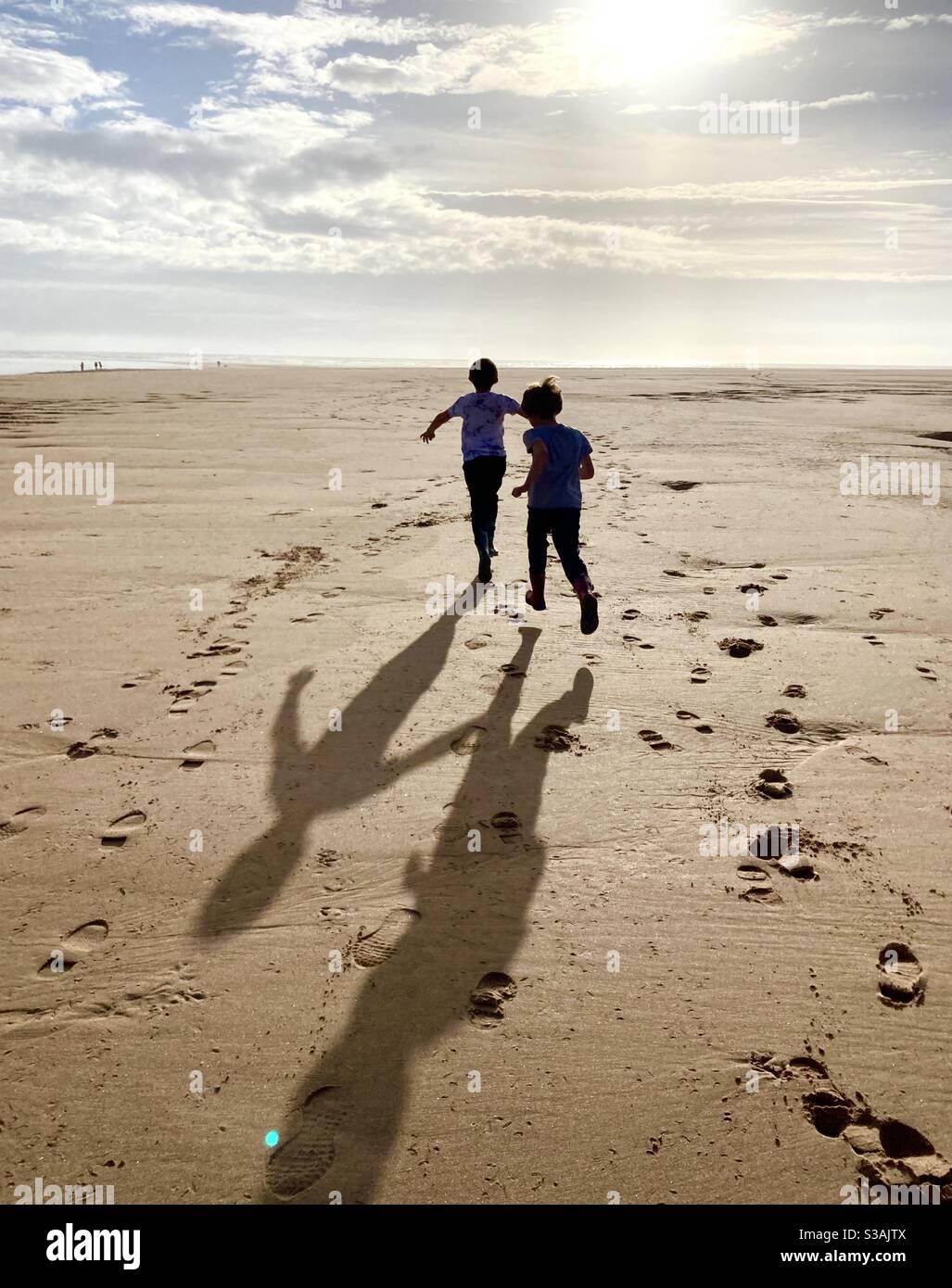 Ragazzi che corrono sulla spiaggia al sole d'autunno con ombre Foto Stock