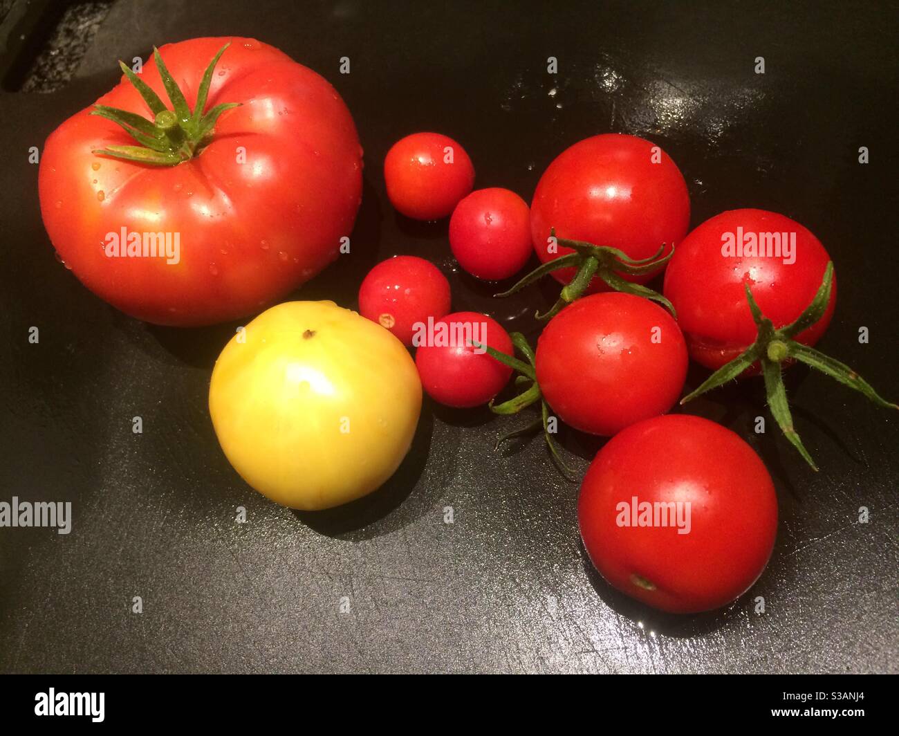 pomodori di varie misure e colori su bordo nero bagnato - Immagine stock catturata con smartphone