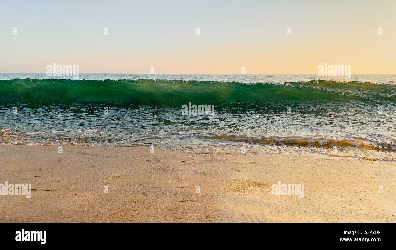 L'oceano si arenata sulla spiaggia di sabbia. Cielo limpido sopra con il sole che tramonta. - Immagine stock catturata con smartphone
