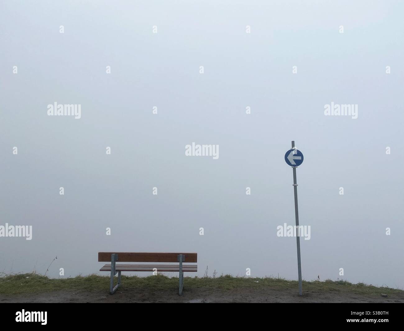 Una panchina e un cartello con una Freccia nella nebbia nelle Alpi tedesche in autunno Foto Stock