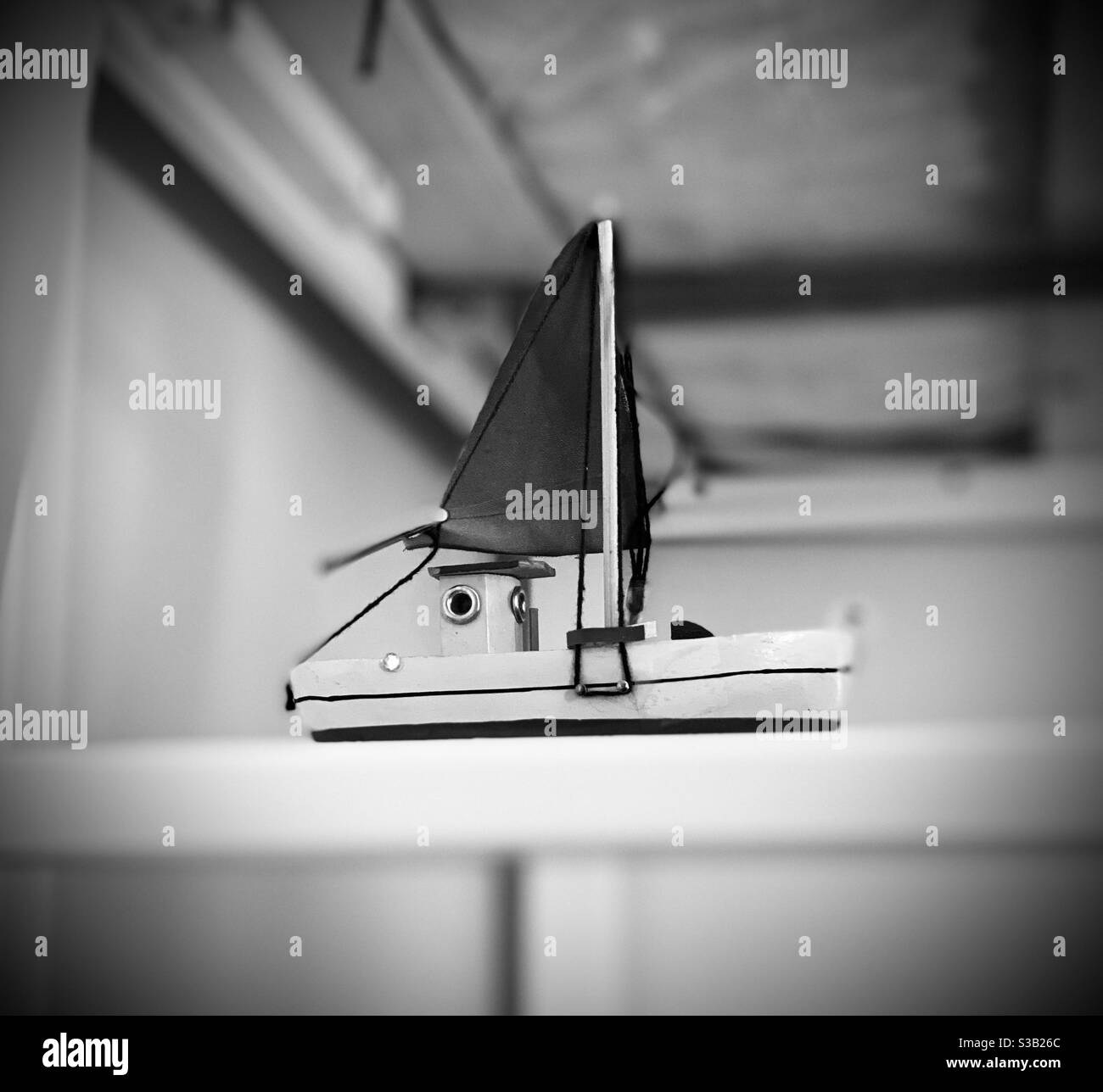 Imbarcazione giocattolo in legno e tessuto su una barra in una stanza bianca in nero e bianco con vignetta. Foto Stock