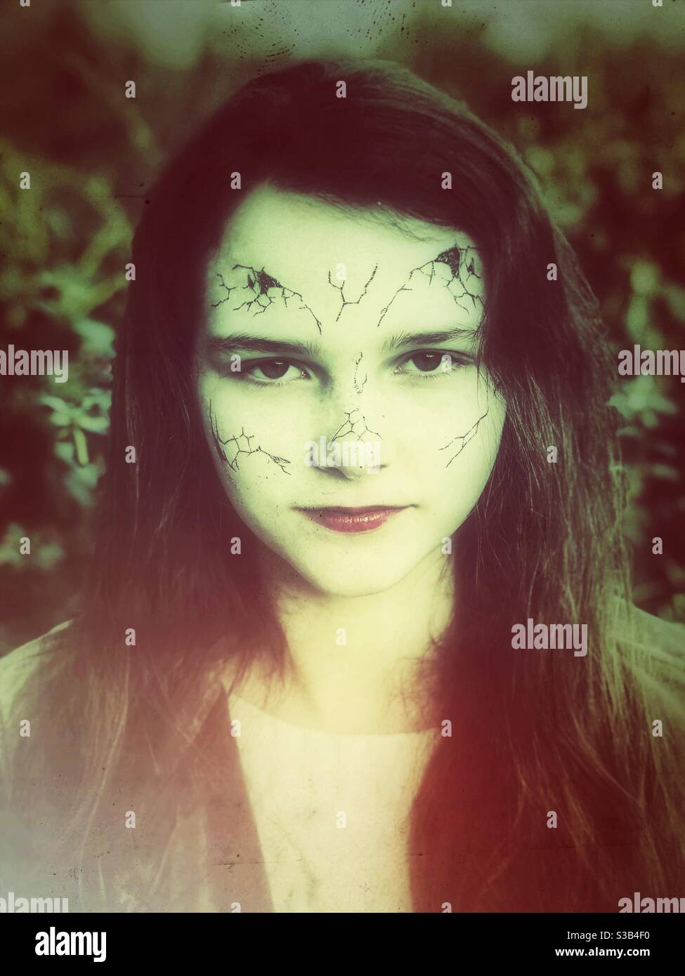 Ragazza teenager con faccia pallida spaccata essendo una porcellana rotta Bambola per Halloween - Immagine stock catturata con smartphone