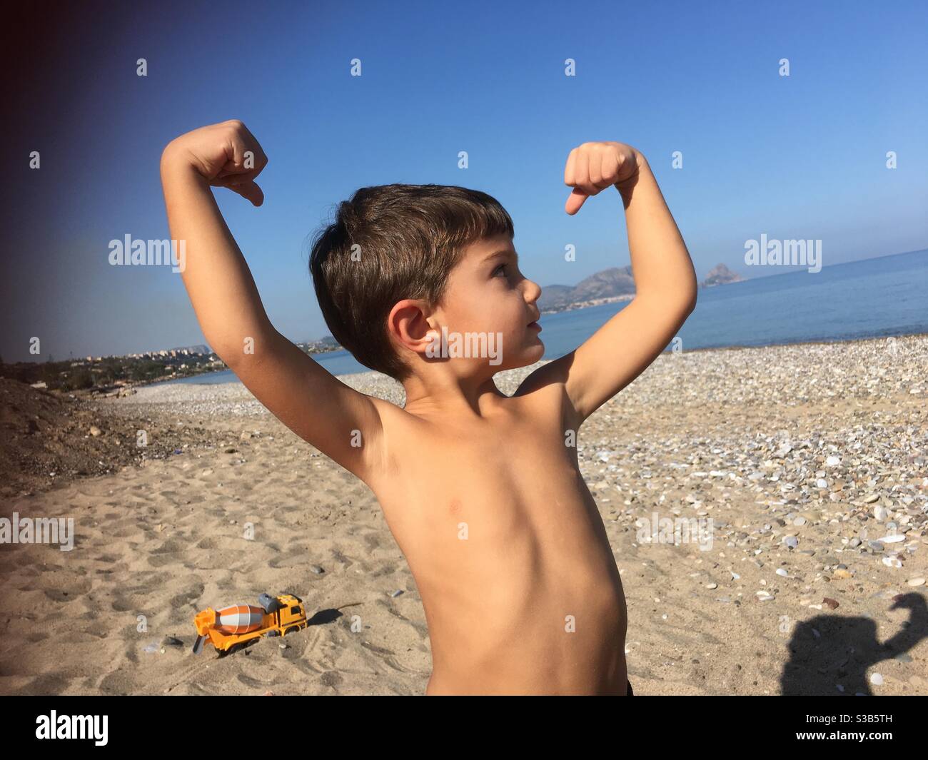 Bambino che mostra i muscoli in spiaggia Foto Stock
