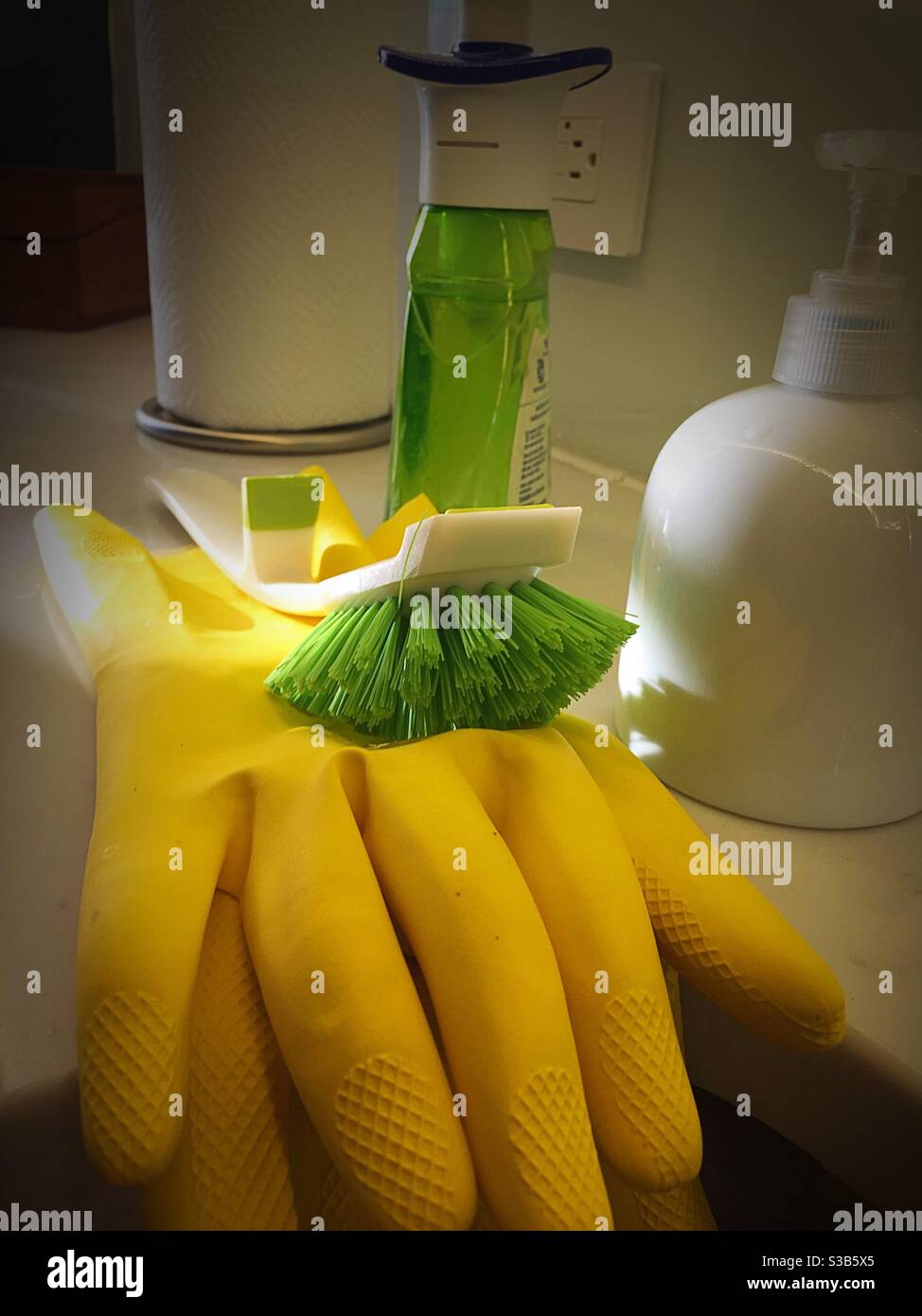 Guanti di gomma gialla, spazzola di pulizia e prodotti su un banco da cucina immacolato negli Stati Uniti con un raggio di sole. Foto Stock