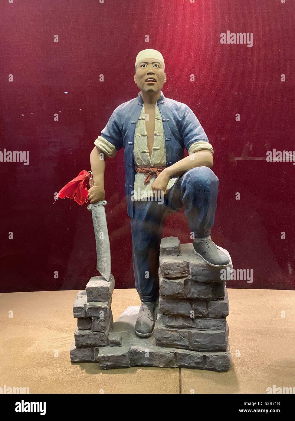 Modello di un personaggio cinese che indossa pantaloni e tunica blu in piedi con una gamba in un muro rotto, tenendo una spada decorata con una bandiera rossa nella mano destra, dal Museo del Cinema di Pechino Foto Stock