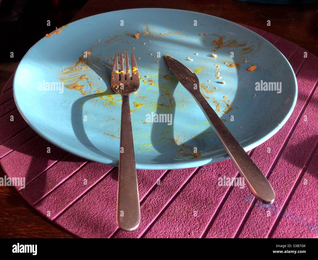 Un piatto blu su una placemat viola, dopo che un fritto in su è stato mangiato Foto Stock