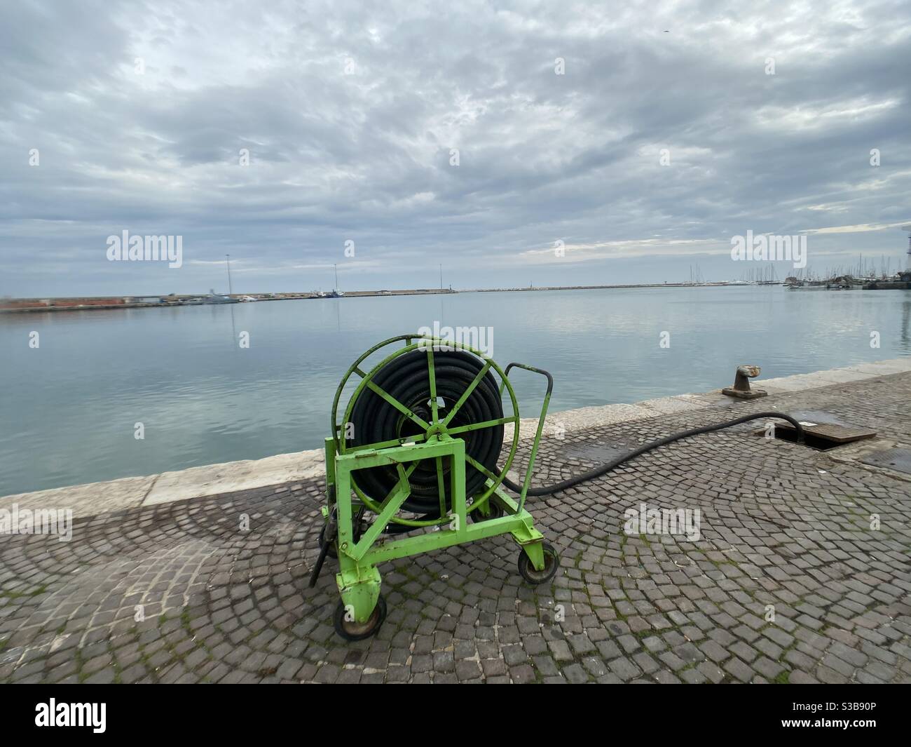 Il tubo dell'acqua rotola su un molo di fronte al porto - Immagine stock catturata con smartphone