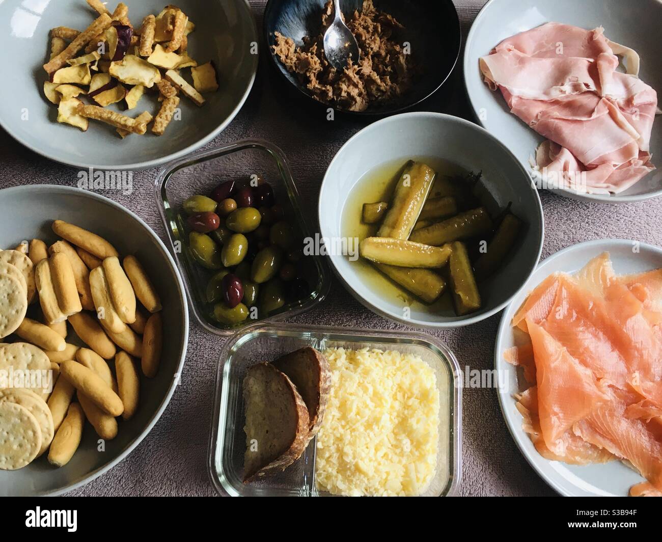 Un bel cesto da pic-nic pronto a mangiare - cetrioli sottaceto, salmone affumicato, prosciutto di Parma, olive, grissini, involtini d'anatra, graffiature di maiale, formaggio grattugiato, pane di pasta acida Foto Stock