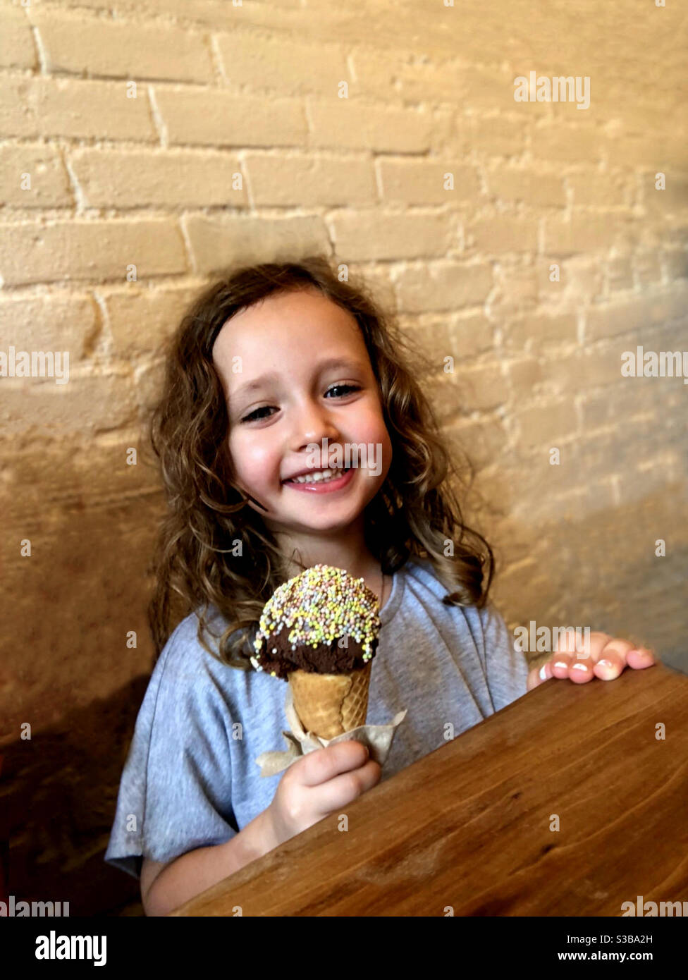 Bambina sorridente e che tiene un cono di crema al cioccolato con spruzzi. Foto Stock