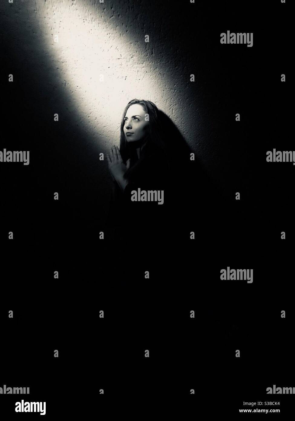 Photographie en noir et blanc d’une femme se tournant vers un rayon de lumière / espoir Foto Stock
