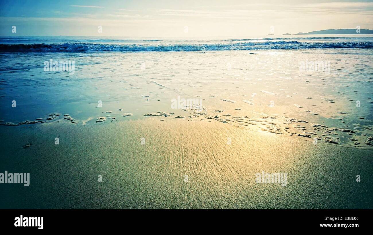 Una fotografia paesaggistica di una spiaggia, piccole onde che entrano con una prospettiva bassa Foto Stock