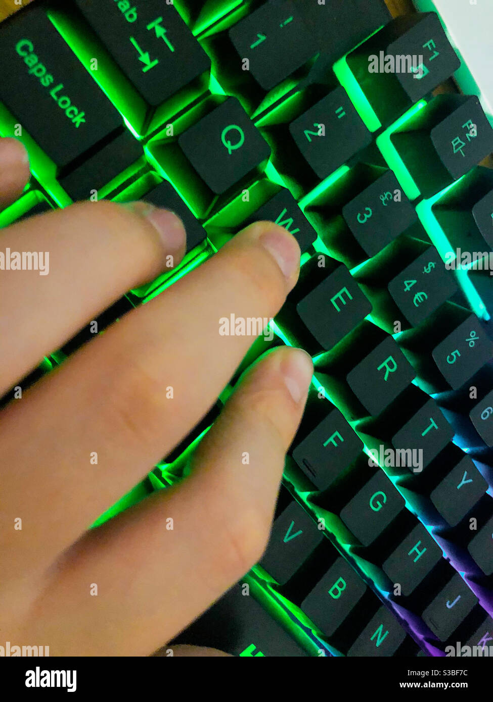La mano del bambino usando una tastiera del computer illuminata. - Immagine stock catturata con smartphone