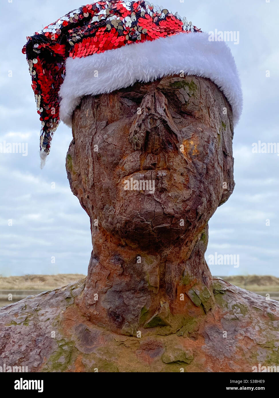 Uno dei cento uomini di ferro di Anthony Gormley un altro luogo reale sculture di dimensioni vive, statue sulla spiaggia di Crosby con un cappello di Natale festivo Foto Stock