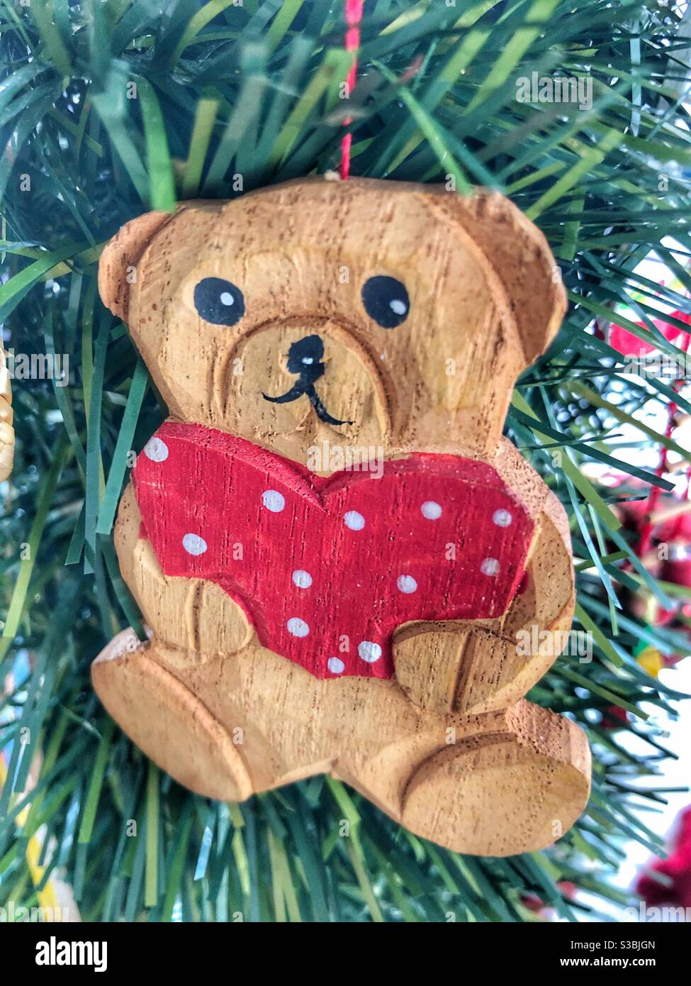 Un orsacchiotto di legno che tiene un cuore rosso appeso su un albero di Natale. - Immagine stock catturata con smartphone