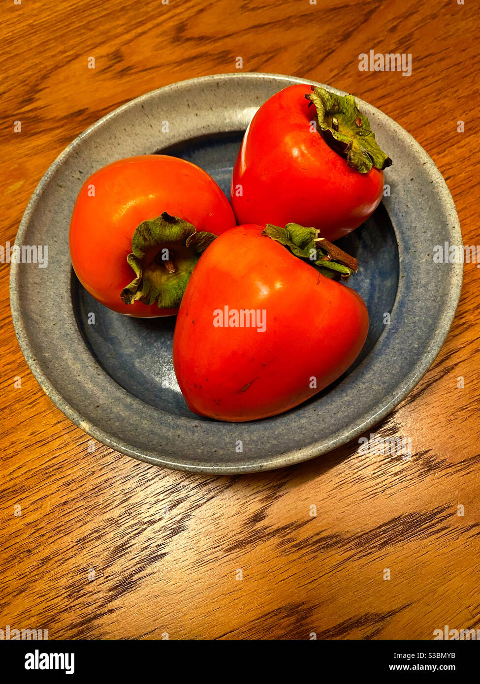 Tre persimmons in un piatto di ceramica - Immagine stock catturata con smartphone