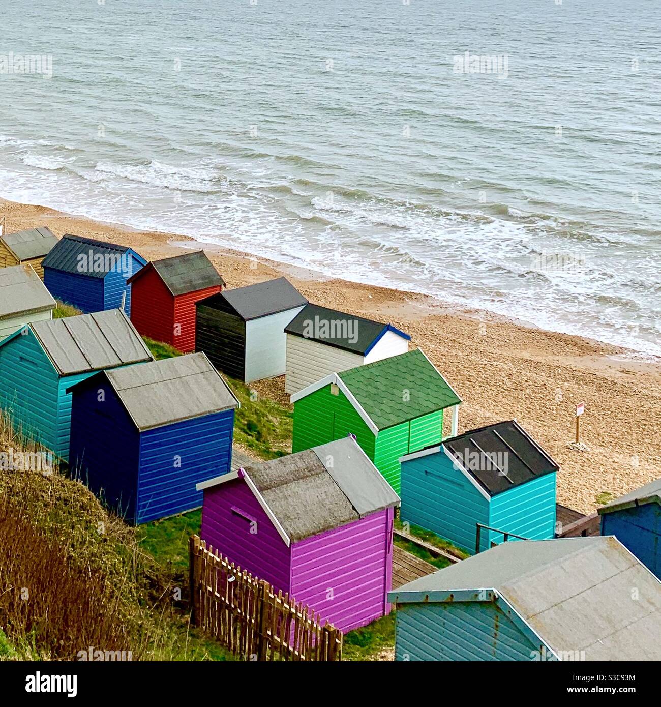 Una jolly giustapposizione di casette da spiaggia dai colori vivaci e casuali sulla costa dell'Hampshire nel Regno Unito Foto Stock