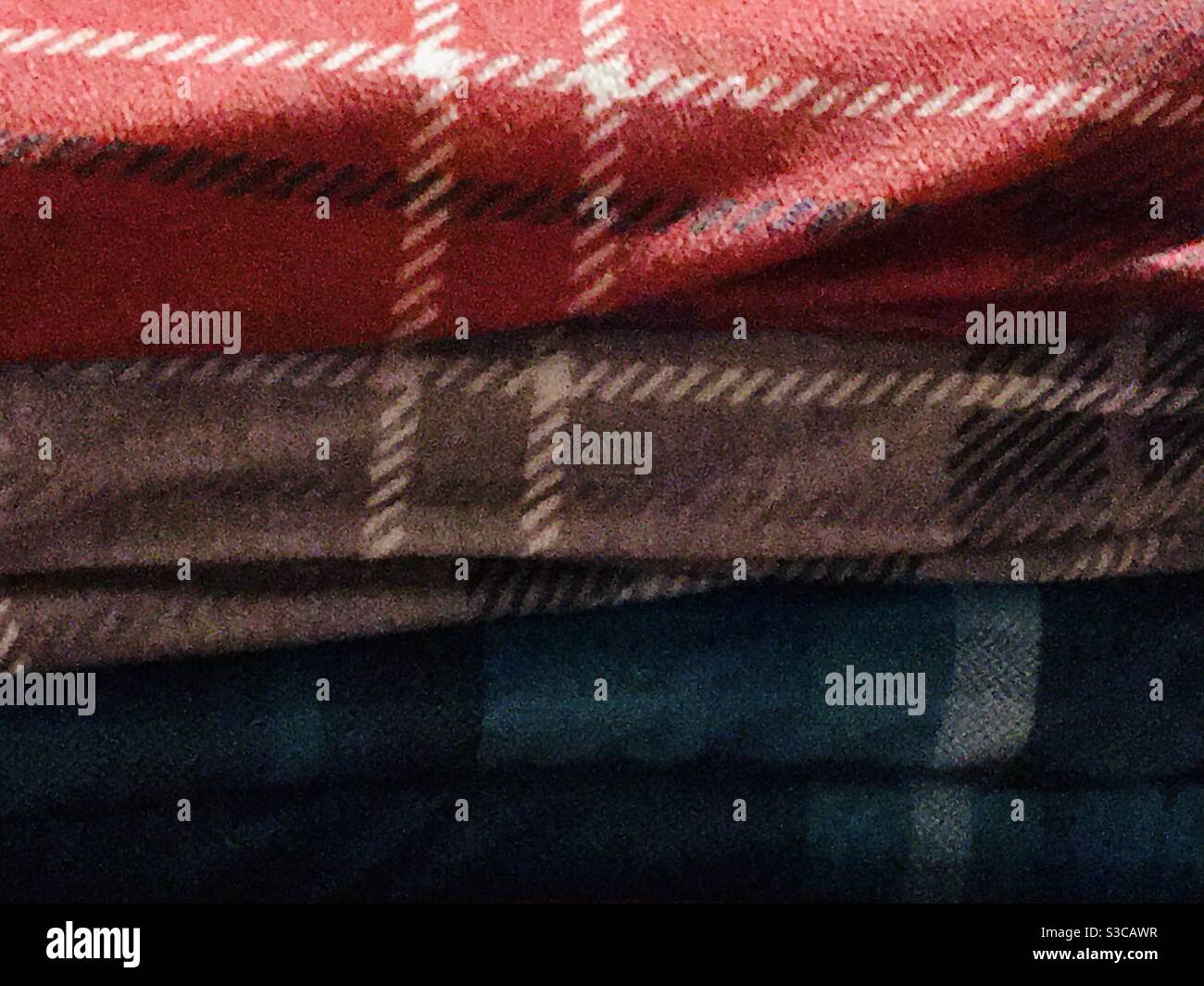 Primo piano di un mucchio di comode coperte di tartan - plaid. Una tettarella, una grigia e una rossa Foto Stock
