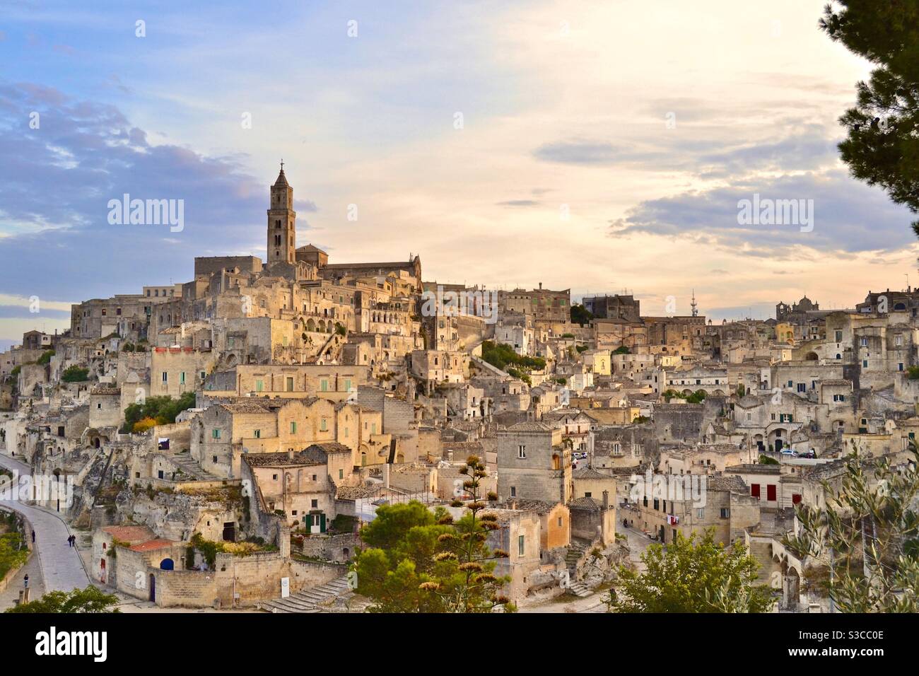 La più magica e bella città collinare antica di Matera Nel sud Italia al tramonto con un cielo morbido opalescente e luce dorata che splende sulle case e sulla chiesa sottostante Foto Stock