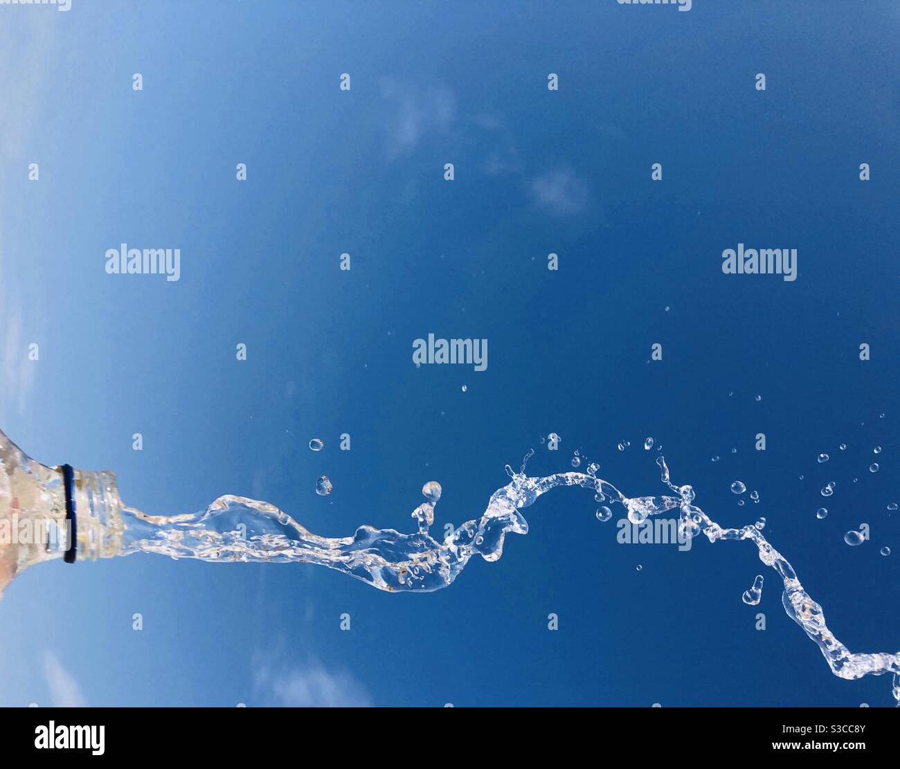 L'acqua si flawing da una bottiglia di vetro contro il cielo blu Foto Stock