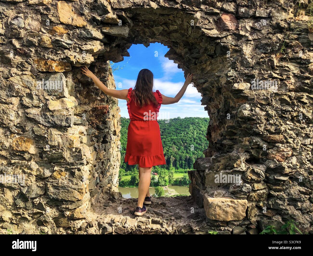 Donna in abito rosso in piedi vicino alla parete di pietra di una vecchia fortezza - Immagine stock catturata con smartphone