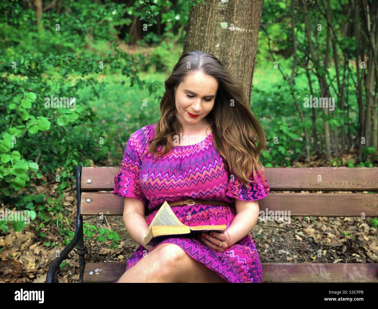 Giovane donna in abito rosa che legge su una panchina Foto Stock