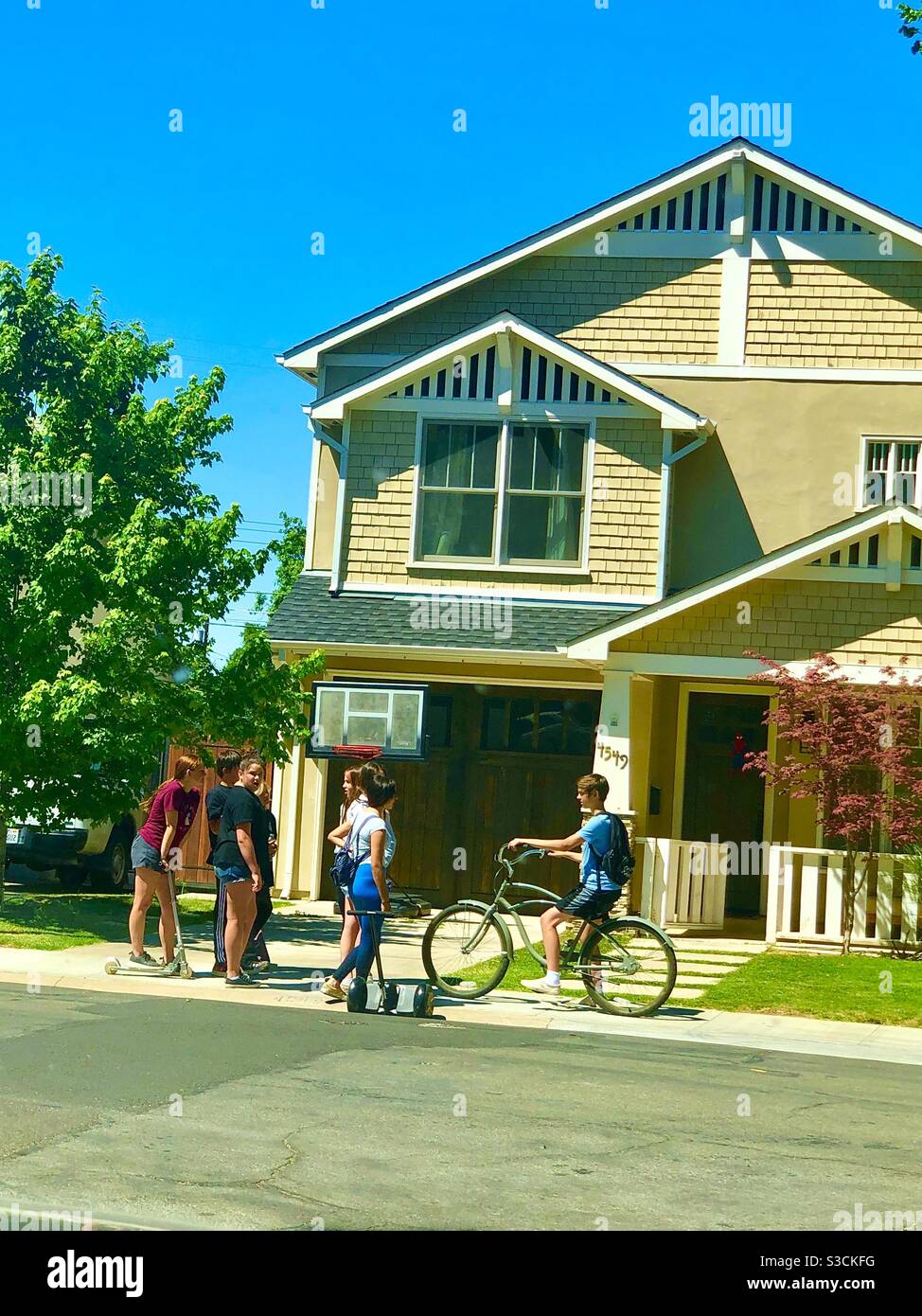 Un quartiere suburbano completamente americano con adolescenti in bicicletta di fronte ad una tipica casa in stile California a Sacramento, Stati Uniti - Immagine stock catturata con smartphone