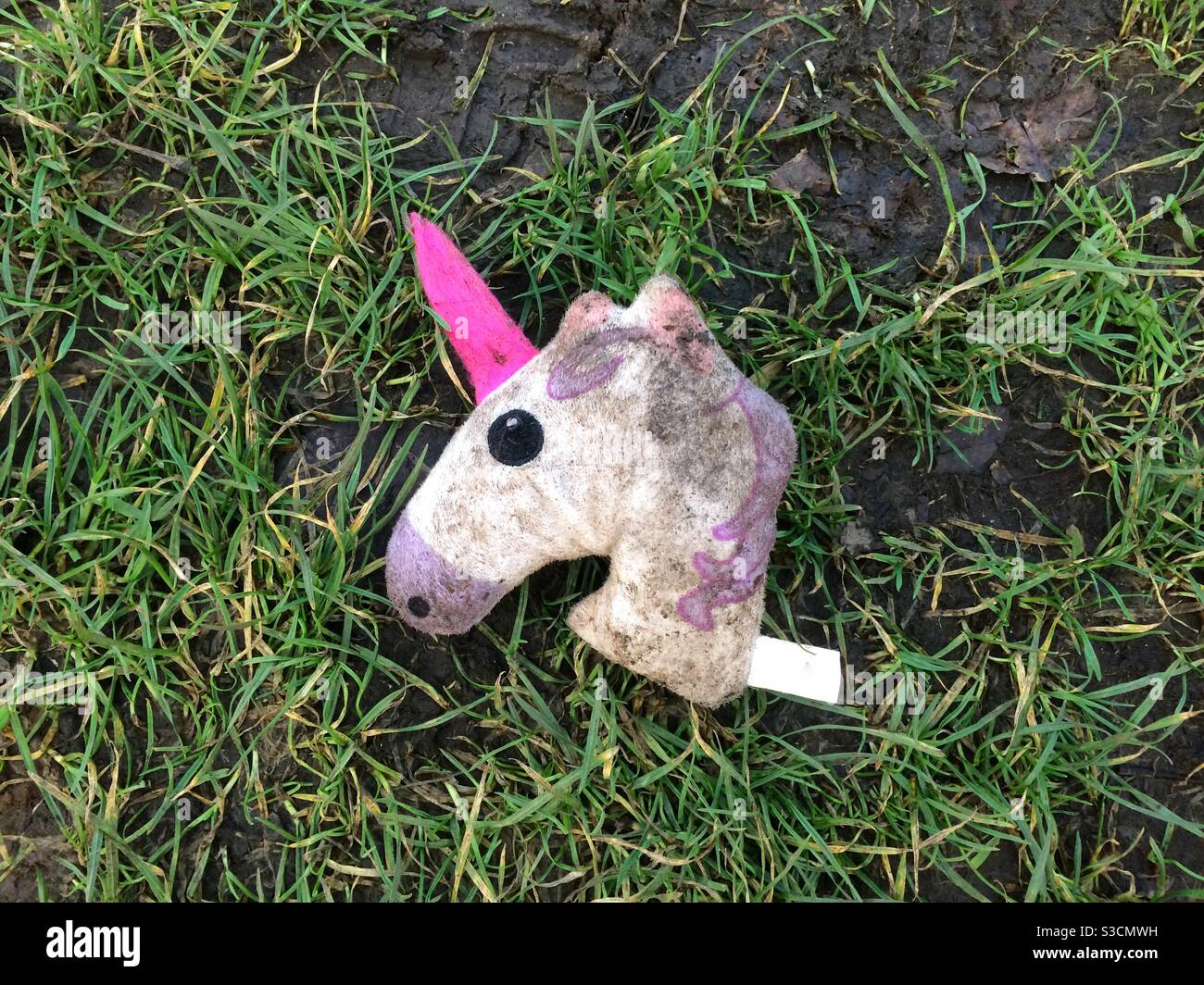 La testa decapitata di un giocattolo farcito unicorno è sporca e abbandonato su erba bagnata Foto Stock