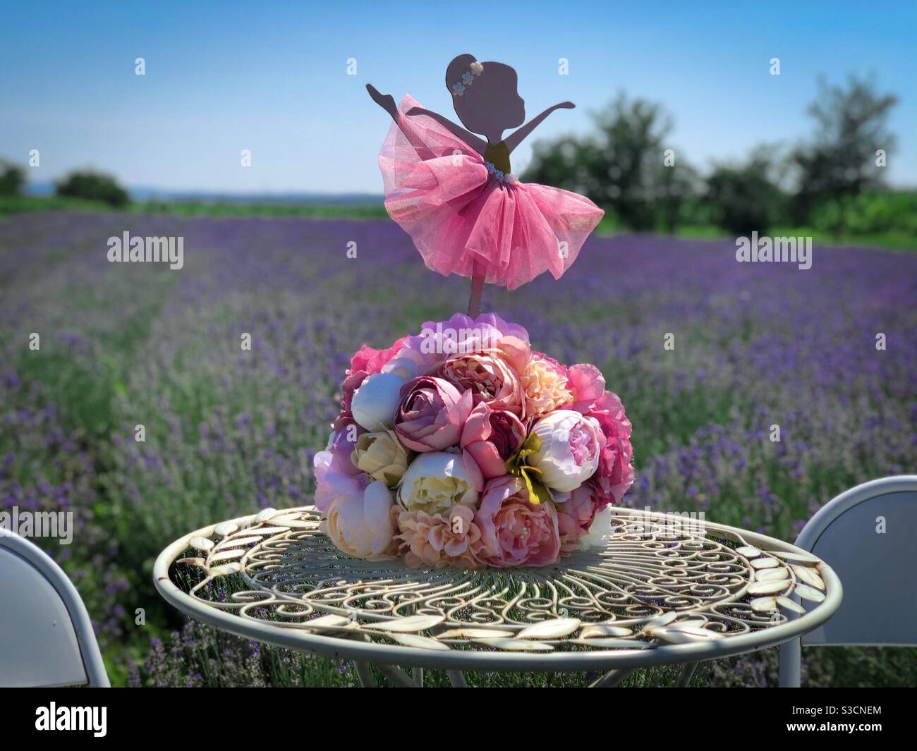 Bouquet di fiori e ballerina decorativa posta su un tavolo in un campo di lavanda - Immagine stock catturata con smartphone