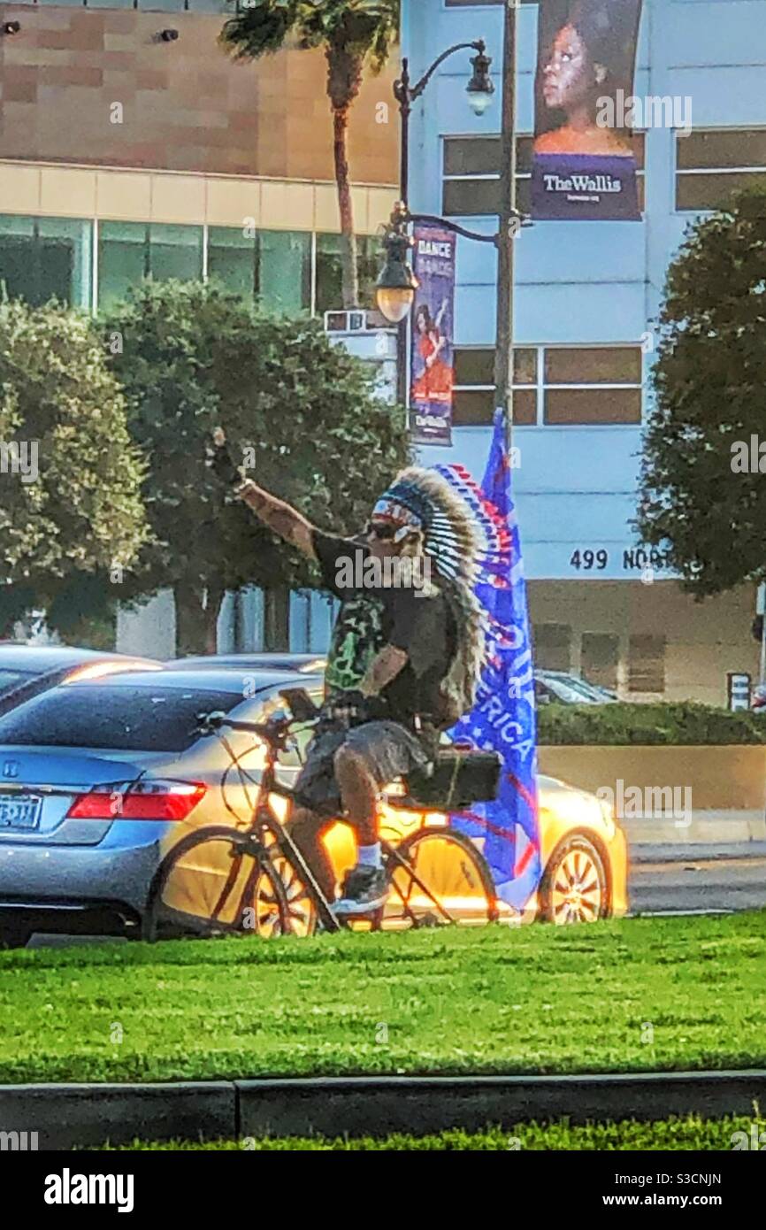 A Los Angeles, non è insolito vedere un uomo in una T-shirt, pantaloncini e un indirizzo indiano a cavallo di una bicicletta e con una bandiera nel mezzo del traffico a Beverly Hills - Immagine stock catturata con smartphone