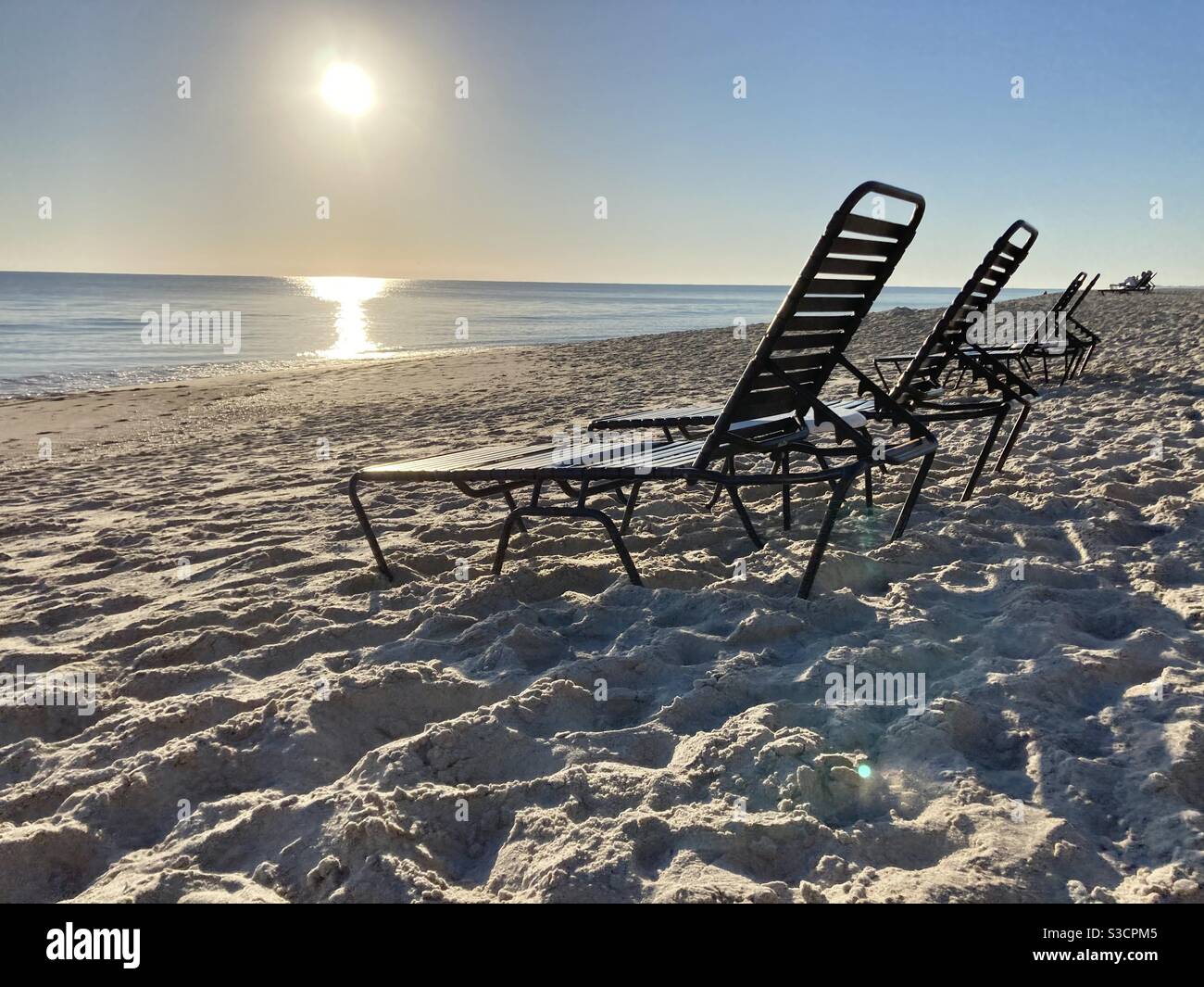 Sedie da spiaggia vuote con il sole che sorge sullo sfondo è acqua molto calma, quasi tutte le onde Foto Stock