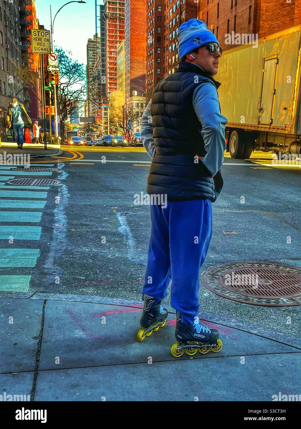Un uomo sulle pale a roller con gli auricolari attende all'intersezione di Park Avenue e 34th St. All'ombra di metà pomeriggio in una fredda giornata invernale nella città di New York, Stati Uniti. - Immagine stock catturata con smartphone