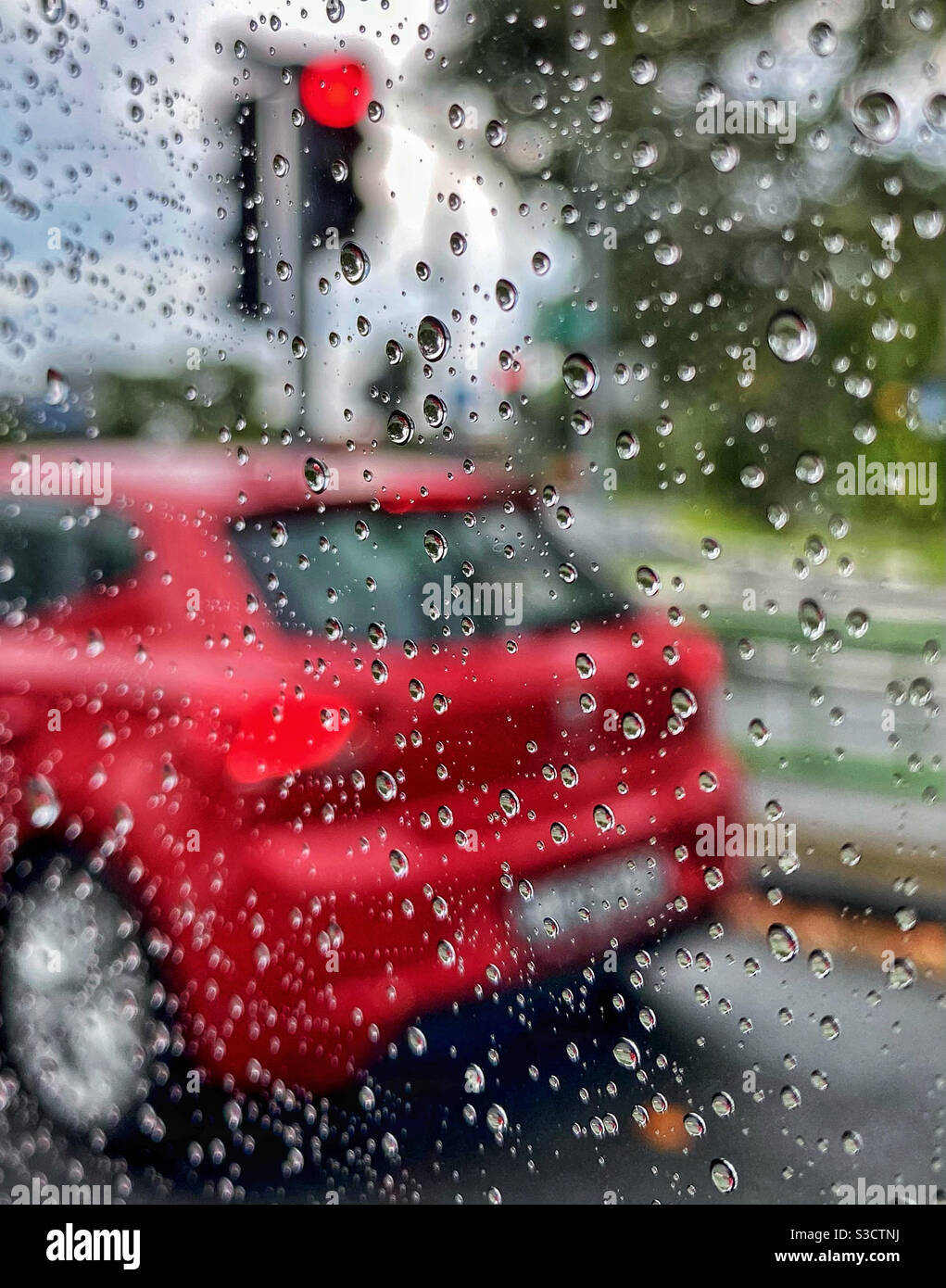 Auto rossa a una luce rossa in una giornata piovosa Foto Stock