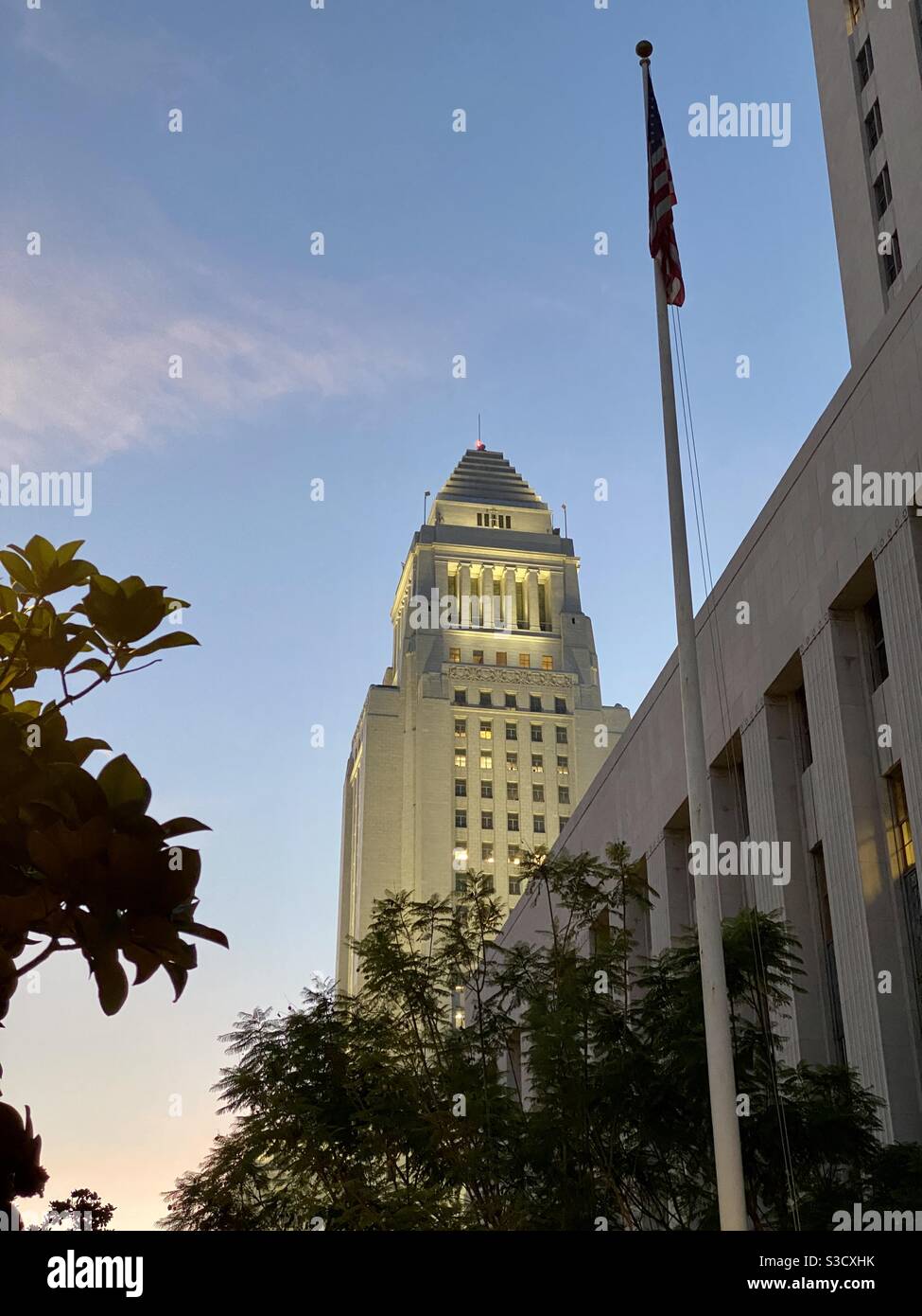 LOS ANGELES, CA, NOVEMBRE 2020: Ampia vista verso il municipio nel quartiere del centro amministrativo del centro città, al crepuscolo con luci dell'edificio visibili e stelle e strisce, bandiera americana in primo piano - Immagine stock catturata con smartphone