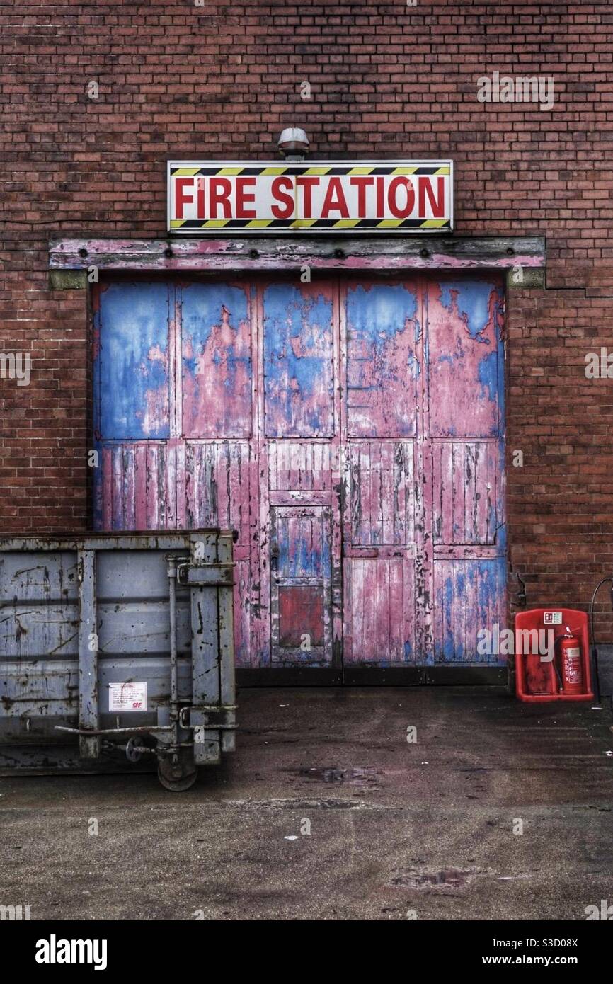 L'ingresso e la porta di un molto vecchio e deserta stazione dei vigili del fuoco con cartello e porta colorata Foto Stock