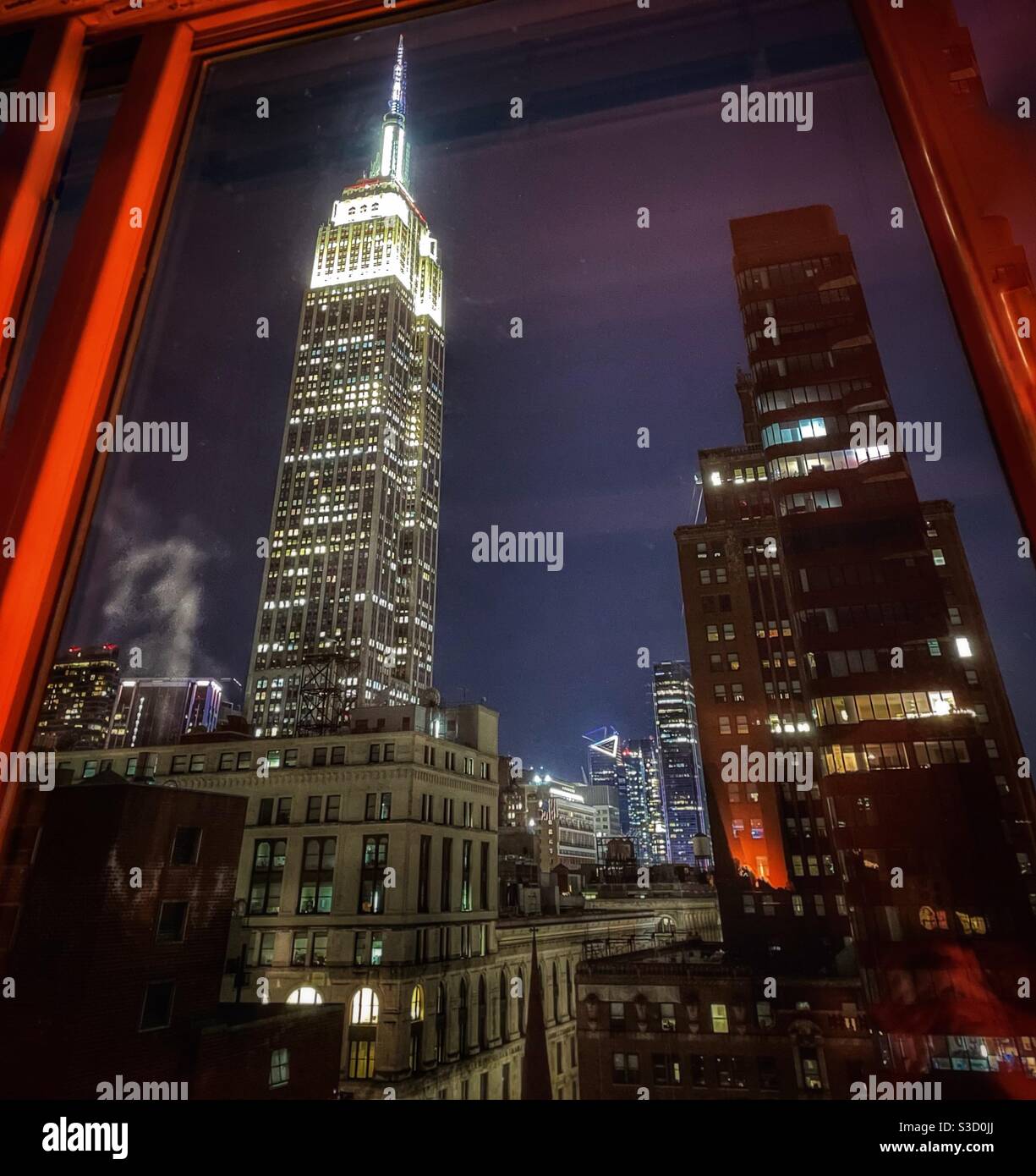 Una serata con vista sulle stalle fuori dalla finestra di un appartamento dei grattacieli di New York City punteggiata dal glamour punto di riferimento Empire state Building illuminato con luci bianche e cantieri Hudson sullo sfondo. - Immagine stock catturata con smartphone