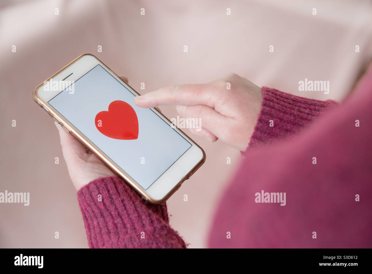 Una sola ragazza che cerca l'amore il giorno di San Valentino toccare un cuore su un'app di incontri sul touchscreen smart telefono Foto Stock