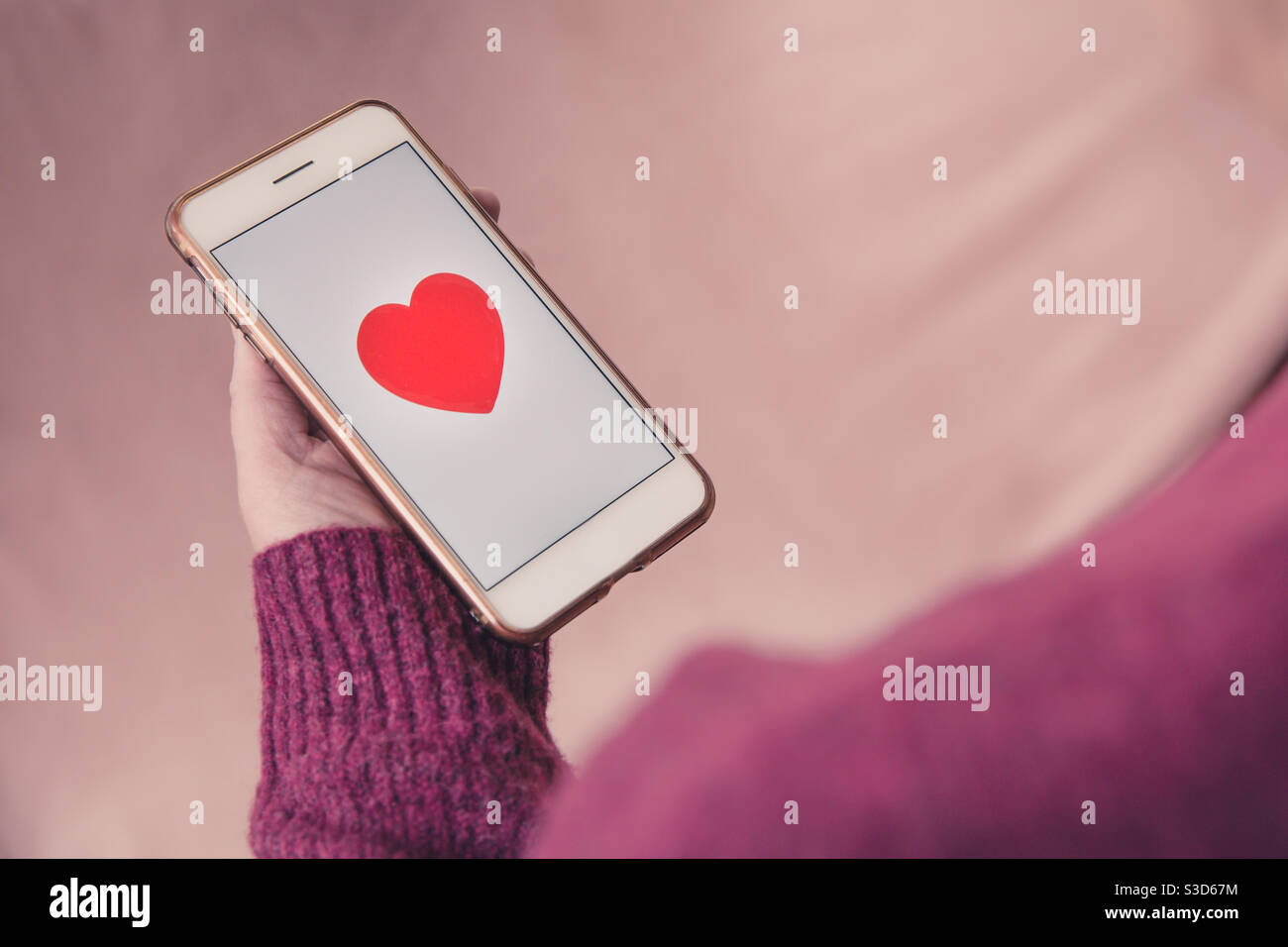Una ragazza singola che tiene il suo telefono cellulare e che cerca amore su un online dating app amore cuore - Immagine stock catturata con smartphone