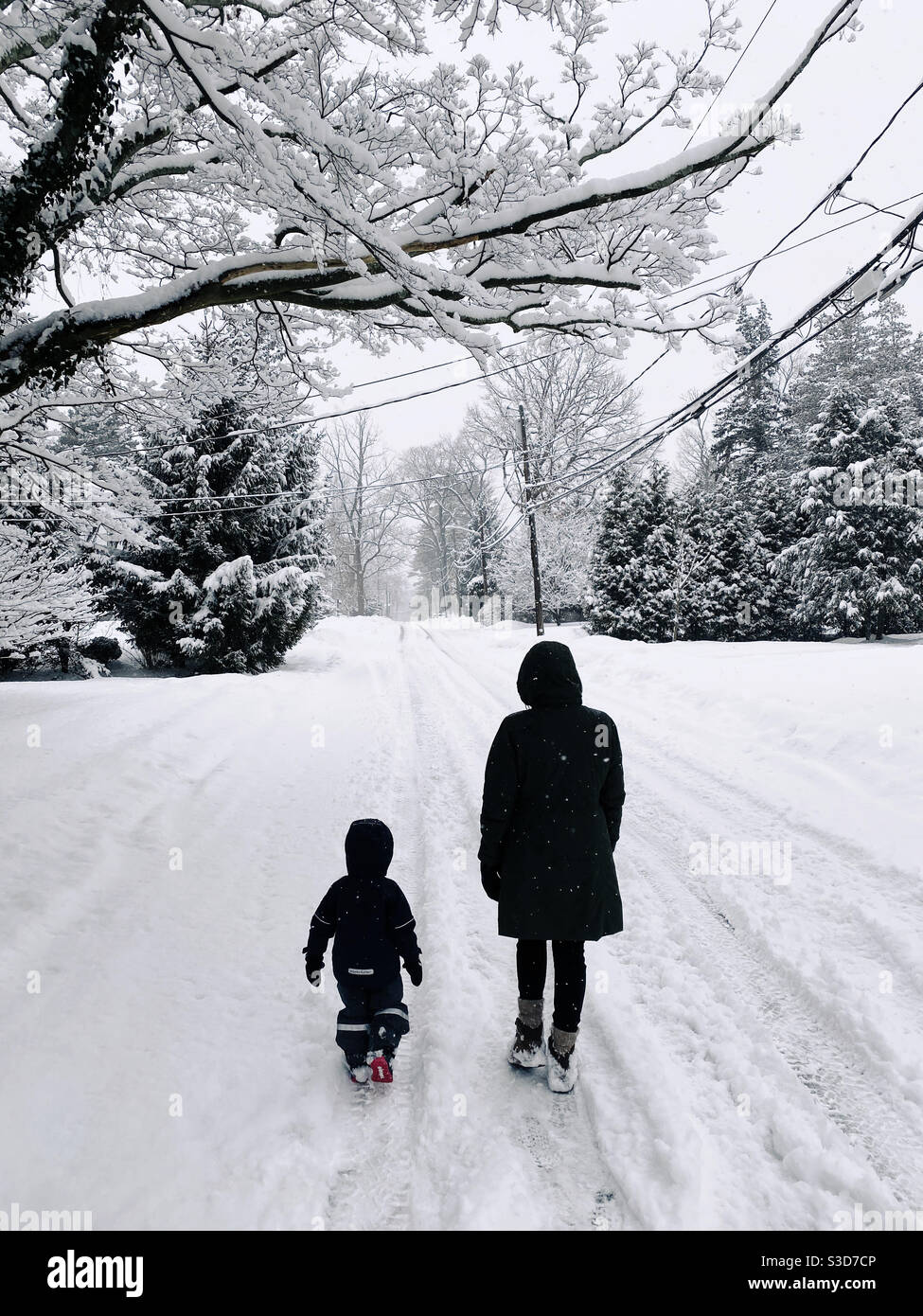 Una madre e un bambino di tre anni camminano insieme lungo una strada innevata durante una nevicata nel New Jersey. Foto Stock