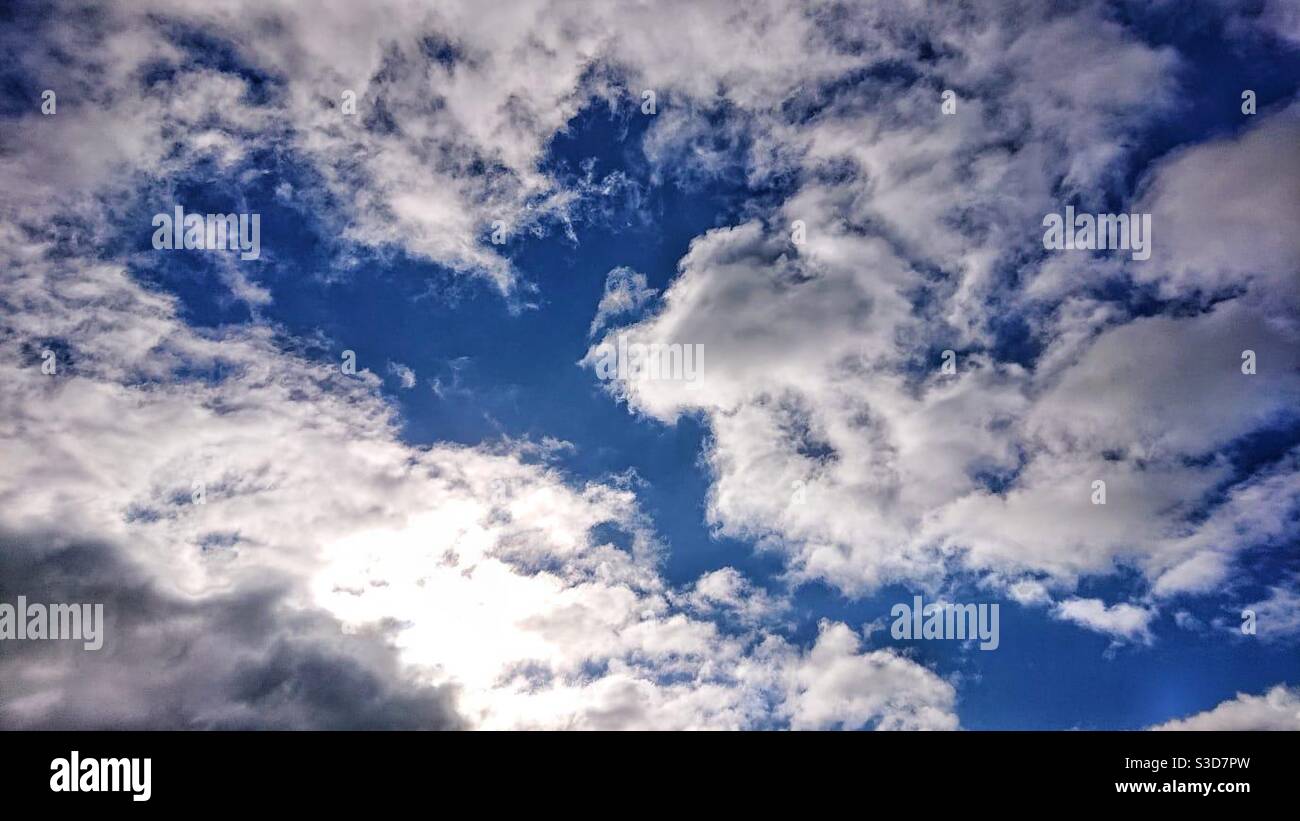 Una fotografia di un cielo blu vivido con un bianco soffio nuvole e luce solare brillante Foto Stock