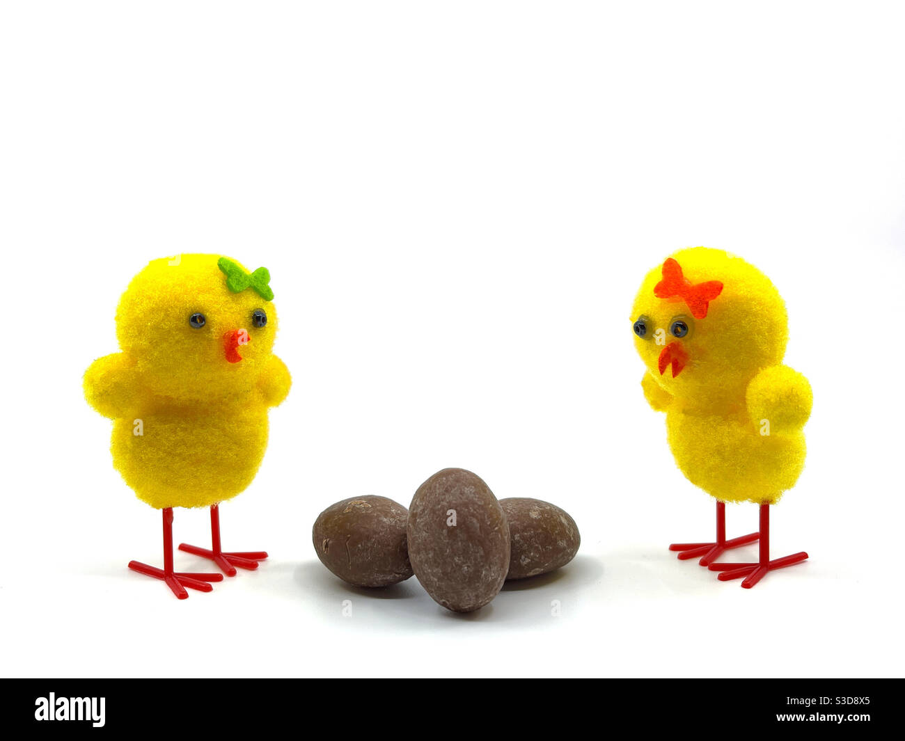 Due pulcini carino modello con piccole uova di Pasqua cioccolato isolato su uno sfondo bianco Foto Stock