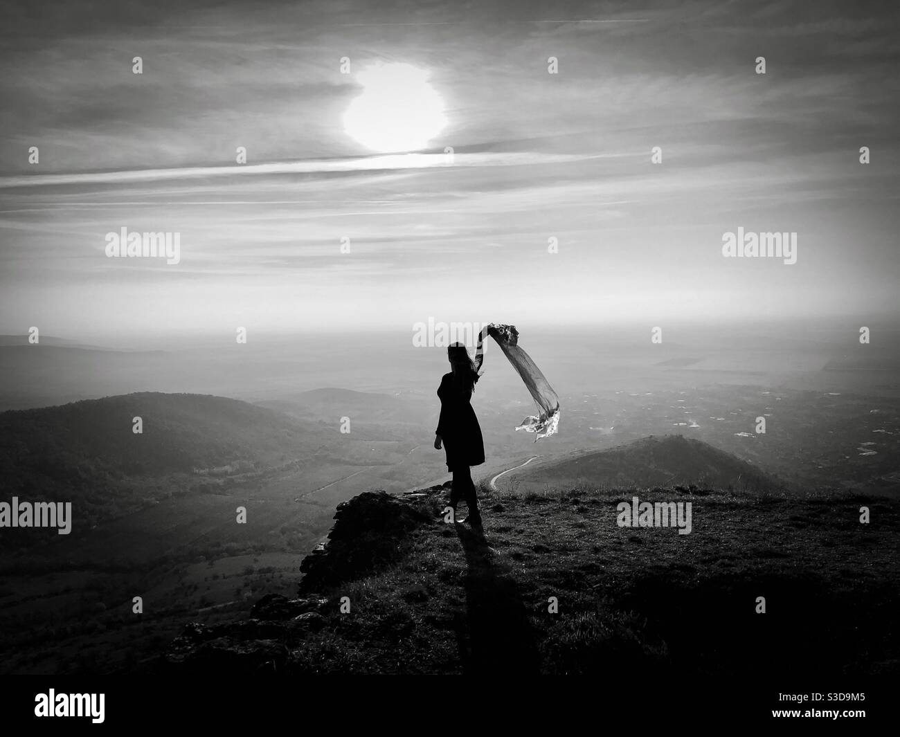 Foto in bianco e nero di donna in piedi sul bordo di una scogliera che tiene una sciarpa che soffia nel vento Foto Stock