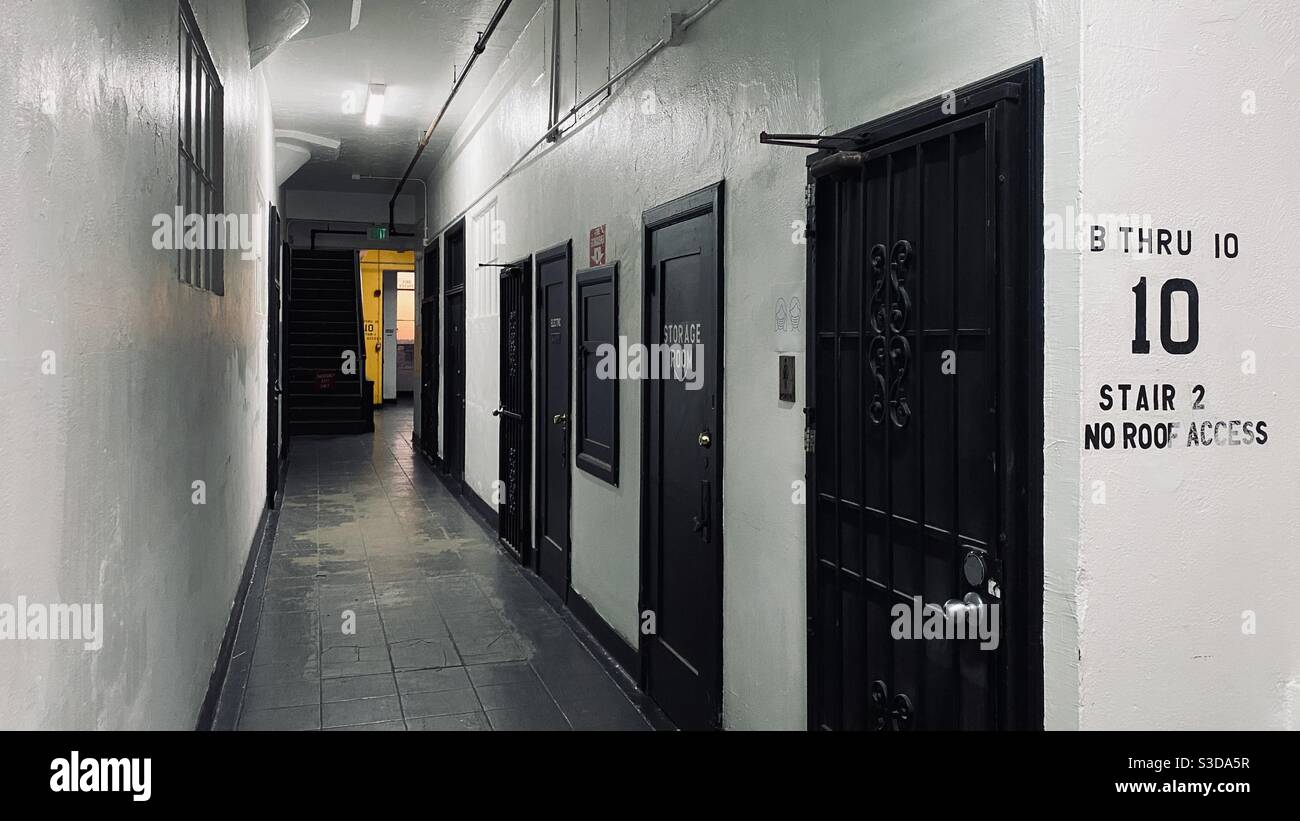 LOS ANGELES, CA, NOVEMBRE 2020: Ampio corridoio interno bianco con vista e porte nere all'interno dell'edificio nel quartiere dei magazzini del centro città con parete gialla all'estremità lontana e tramonto attraverso la finestra Foto Stock