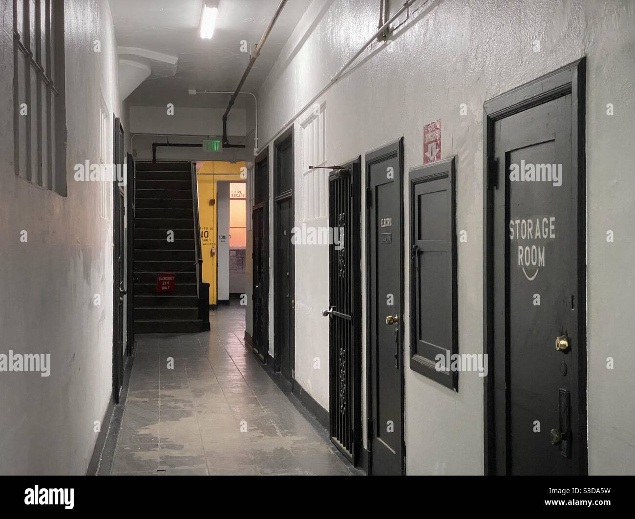 LOS ANGELES, CA, NOVEMBRE 2020: Corridoio interno bianco con porte nere all'interno dell'edificio nel quartiere dei magazzini del centro, parete gialla all'estremità lontana e tramonto che passa attraverso la finestra - Immagine stock catturata con smartphone