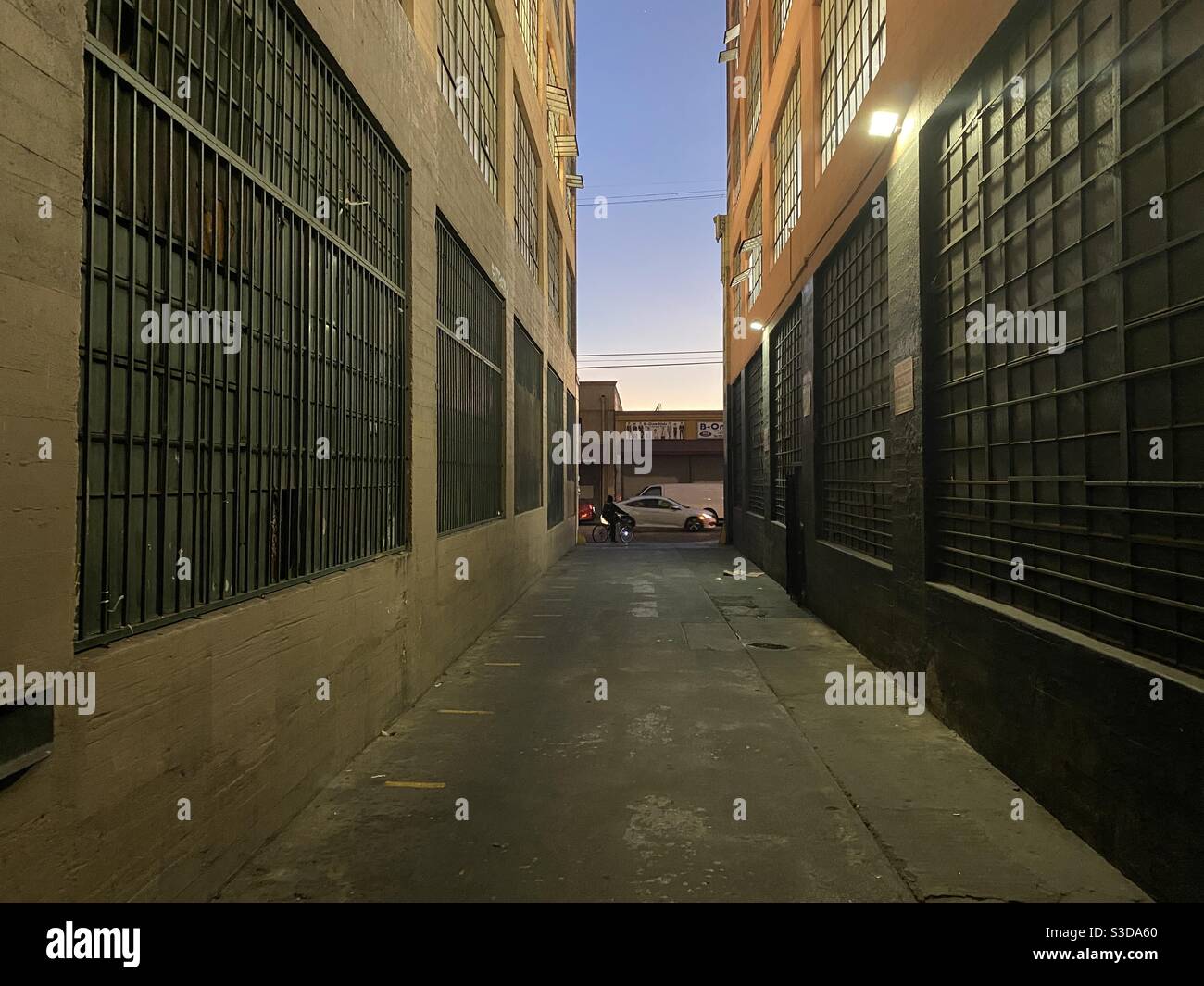 LOS ANGELES, CA, NOVEMBRE 2020: Vicolo vuoto con ciclista e traffico che passa all'estremità lontana, tra vecchi edifici commerciali e industriali nel distretto di magazzino del centro al crepuscolo Foto Stock