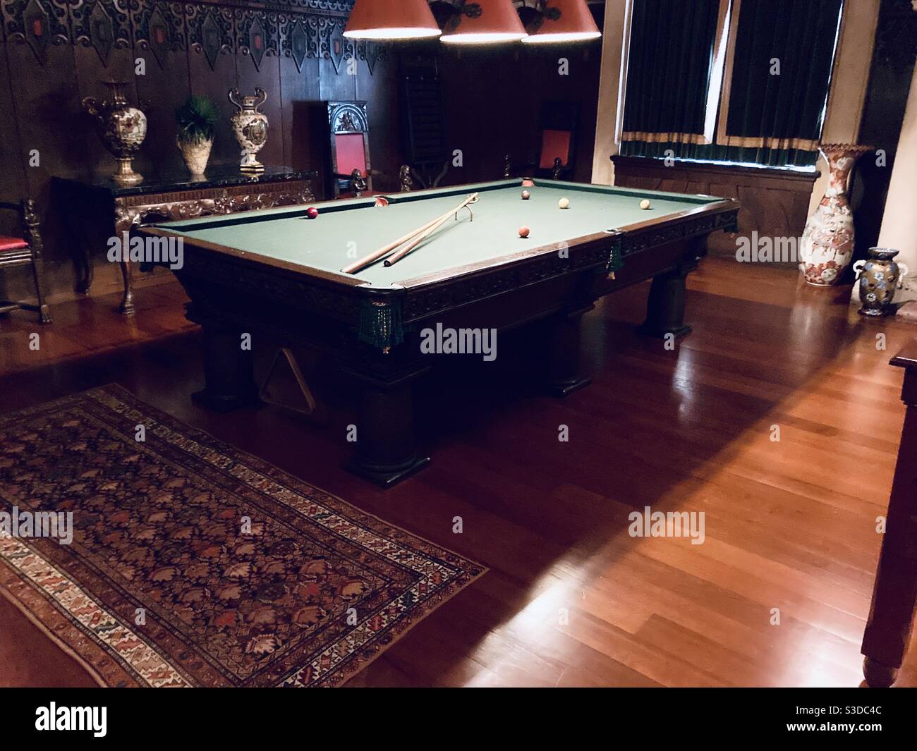Una classica immagine della sala biliardo un tavolo da biliardo in una sala di legno scuro. Due spunti da biliardo sul tavolo insieme a palline colorate pronte per una partita - Immagine stock catturata con smartphone