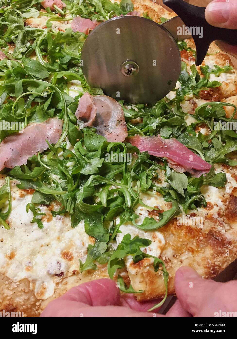 Uomo tagliando una pizza gourmet con una ruota di metallo per pizza, Stati Uniti Foto Stock