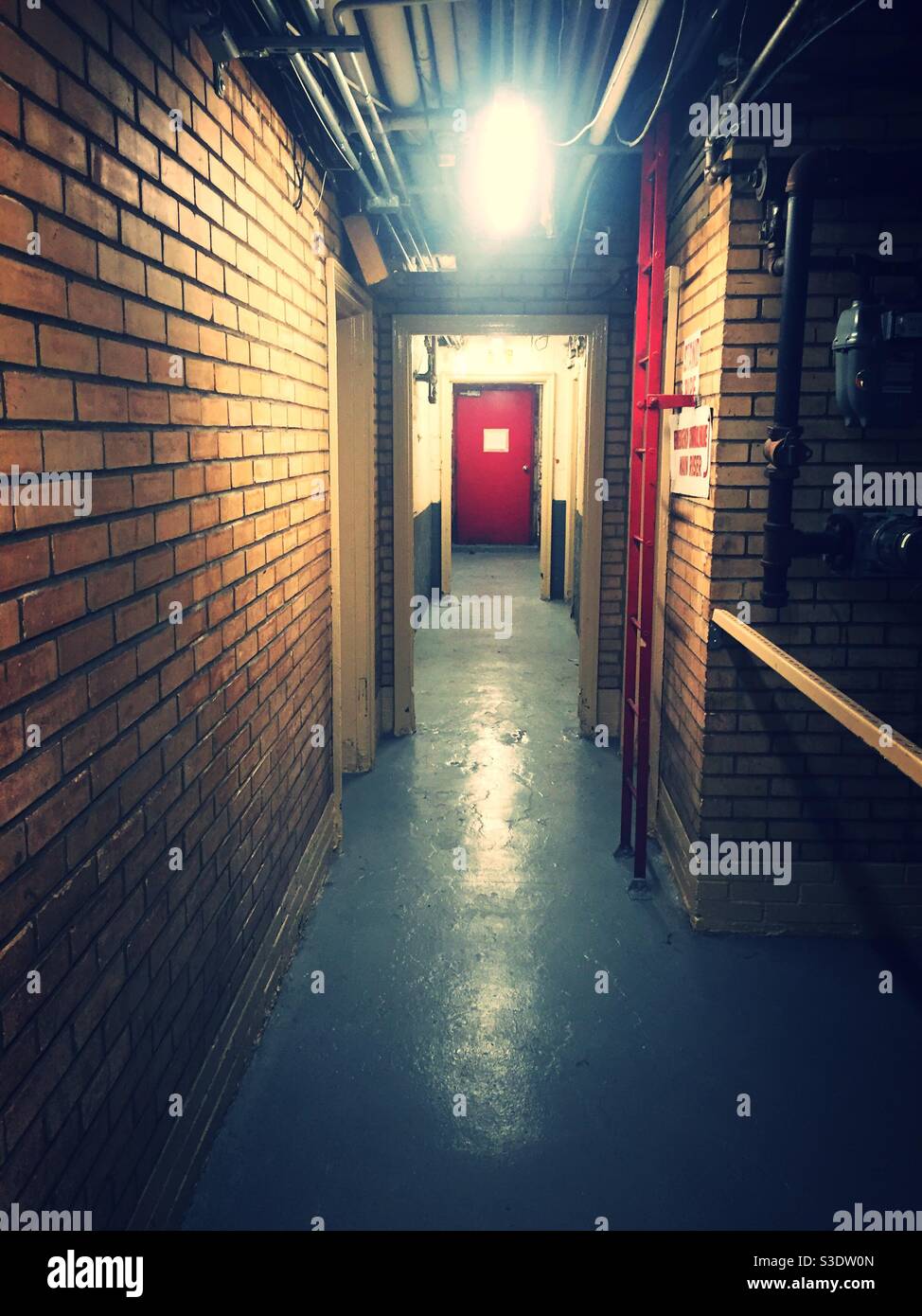 Lungo corridoio seminterrato con una porta rossa alla fine in un edificio di appartamenti a New York City, USA - Immagine stock catturata con smartphone